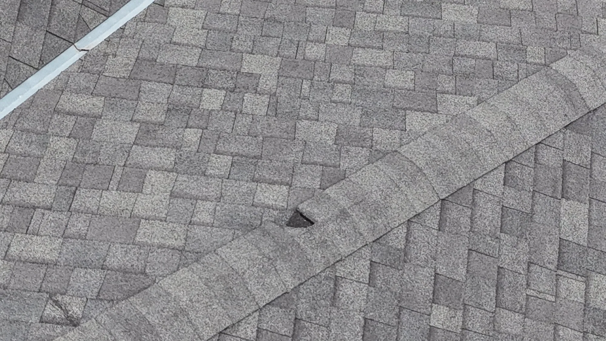 Close-up of a torn and displaced asphalt shingle near a roof ridge on a New Orleans home