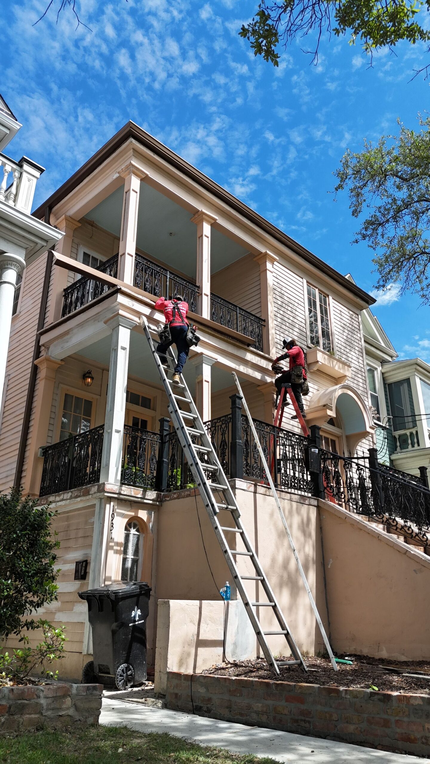 GuttersTech crew working from extension ladders on the eaves of a historic New Orleans building with ornate iron balconies