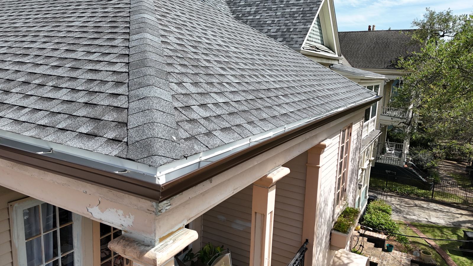 Corner view of a historic New Orleans area home showing a new shingle roof, gutter, and siding