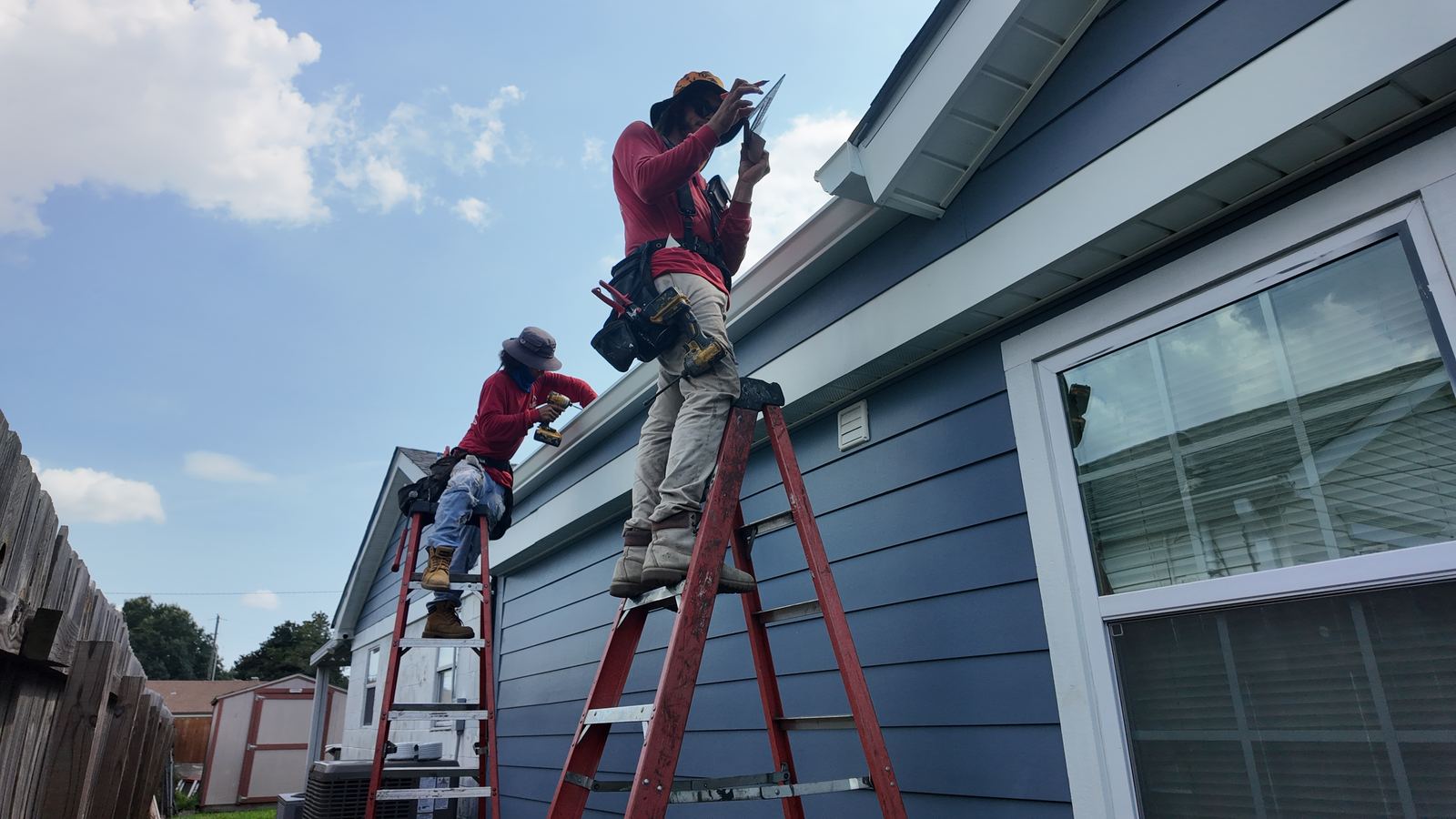 GuttersTech technician on a ladder fitting a seamless gutter along the roofline of a New Orleans area home