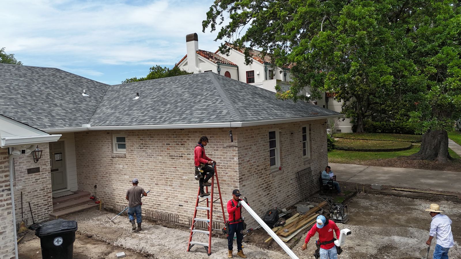 A GuttersTech crew laying out new seamless gutter sections on site at a brick New Orleans area home before installation